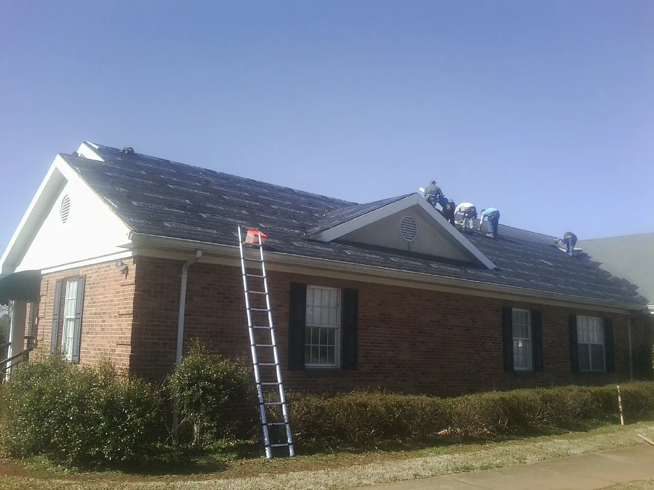 Crew tearing shingles off a brick ranch roof with a ladder set — Emergency Roof Repair work by our crew in Paris
