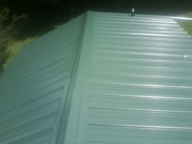 New green metal panels meeting at the ridge of a roof — Flat Roof Repair work by our crew in Paris